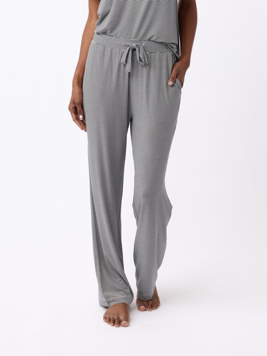A person is standing barefoot against a white background, wearing Cozy Earth's Women's Bamboo Stretch-Knit Pant in a gray-striped design with a drawstring waist and relaxed fit for comfort. |Color:Eclipse Mini Stripe