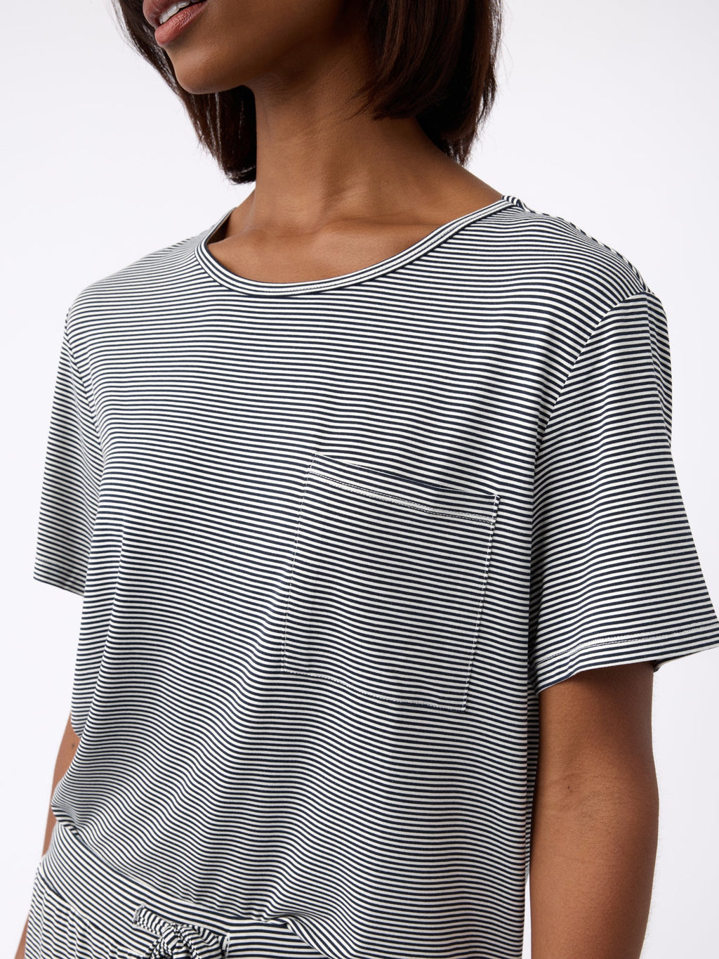A person wearing Cozy Earth's Women's Bamboo Stretch-Knit Lounge Tee in black and white stripes with a pocket, featuring short sleeves and a round neckline against a plain white background. |Color:Eclipse Mini Stripe