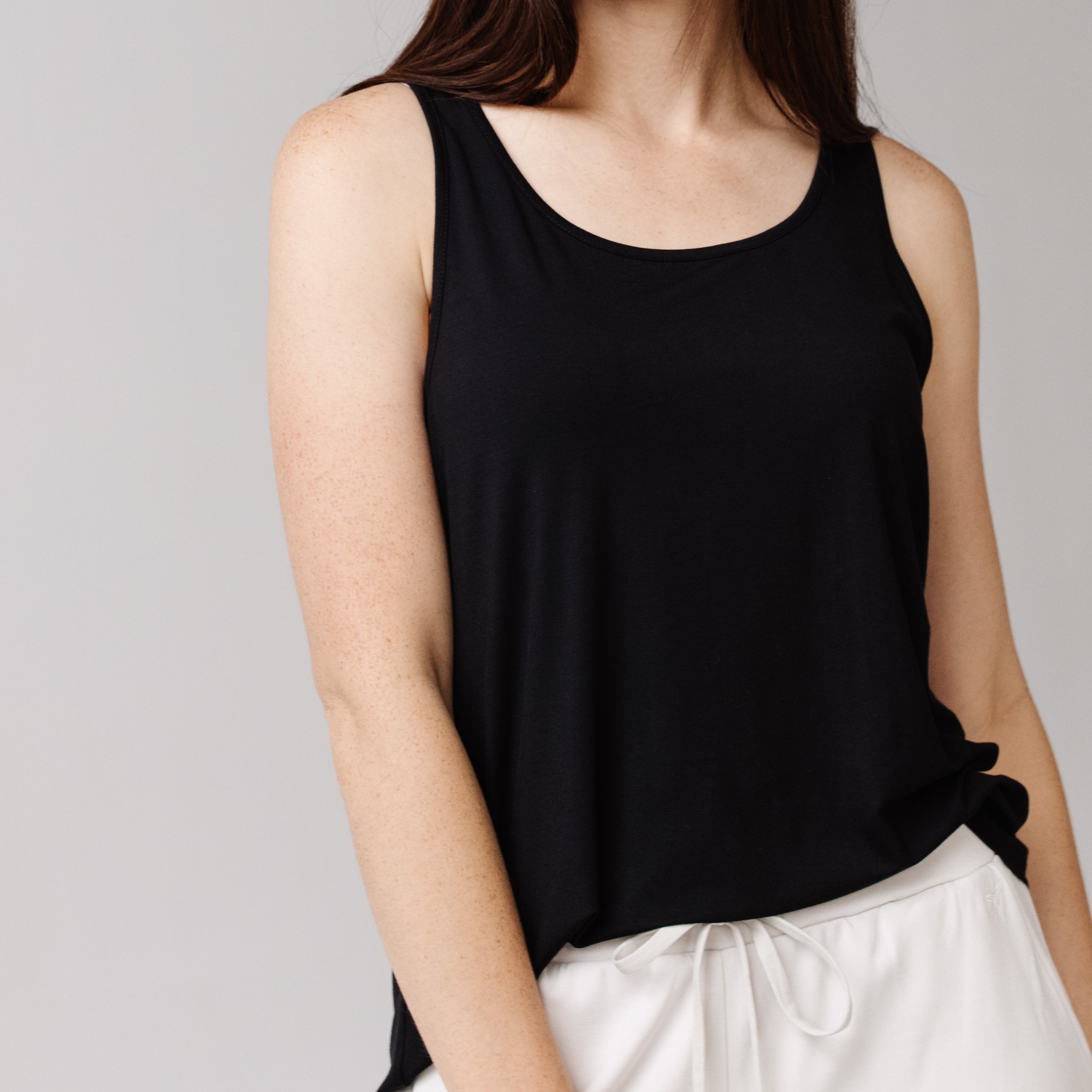 Woman in a black Cozy Earth Stretch Knit Tank and white shorts is shown from the neck down with a neutral background |Color:Black
