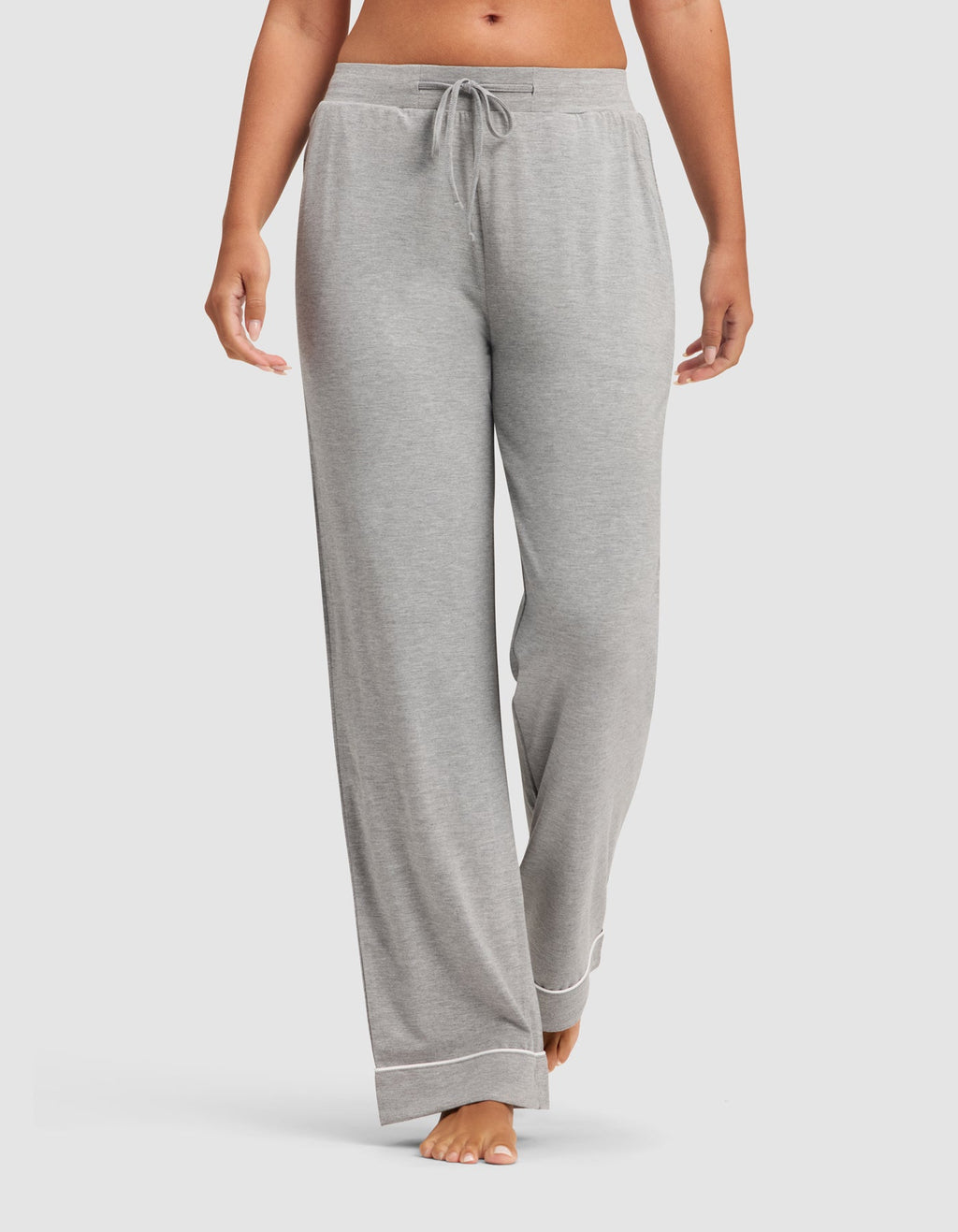 A woman models the HIDE Women's Bamboo Stretch-Knit Pajama Pant in light grey, featuring a drawstring waistband and white hem trim, standing barefoot against a plain white background. |Color:Grey