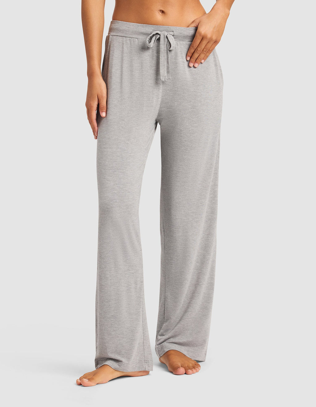 A woman models the Cozy Earth Women's Bamboo Stretch-Knit Pant in light gray, shown barefoot from the waist down against a plain white background. Only her lower torso and legs are visible.|Color:Heather Grey