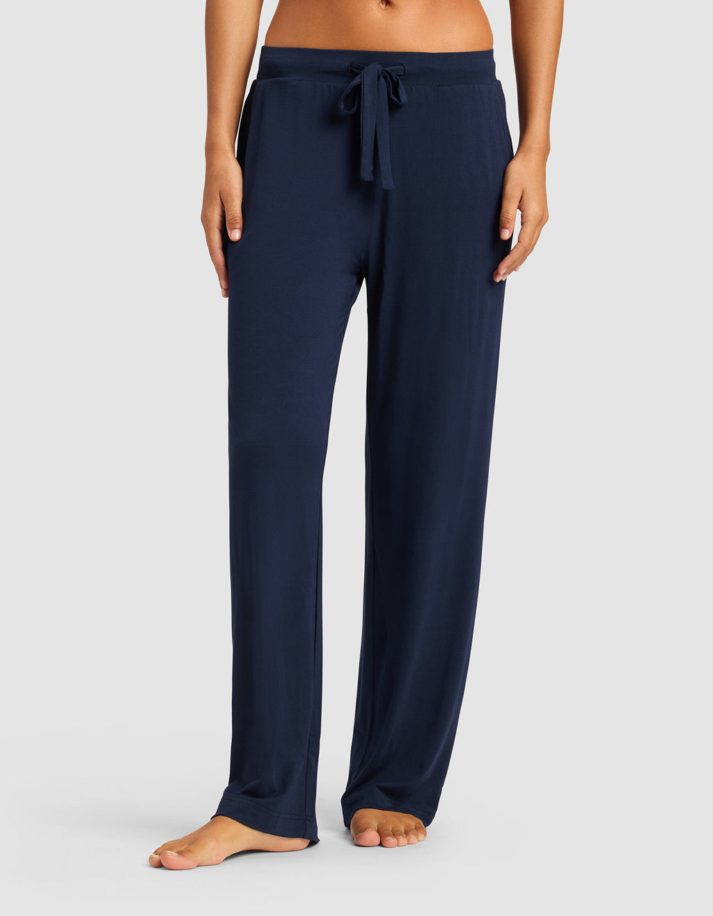 Model wears Cozy Earth Women’s Bamboo Stretch-Knit Pant in navy blue, featuring a loose fit and drawstring waist, shown barefoot with only the lower torso and legs visible against a light gray background.|Color:Navy